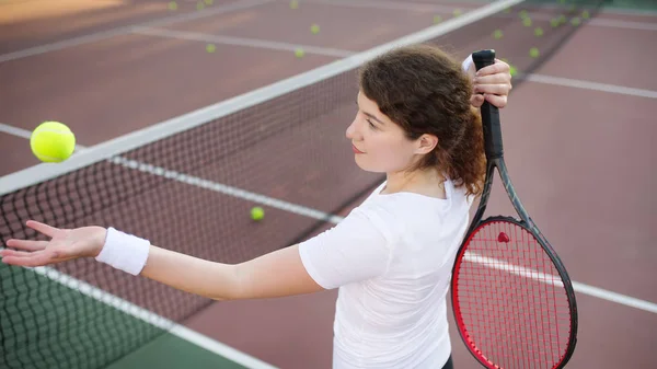 Young female tennis player with tennis ball and racket preparing to serve. Girl on tennis court