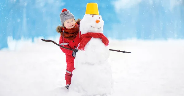 雪だるまを楽しんで赤冬の服の少年 冬の子どもたちとアクティブなアウトドア レジャー 雪に覆われた冬の公園で散歩中に子供します — ストック写真