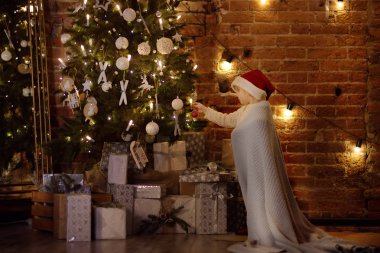 Küçük çocuk giyen Noel Baba şapkası için hazır Noel kutlaması. Şirin çocuk mor cam oyuncak ile Noel ağacı süsleme