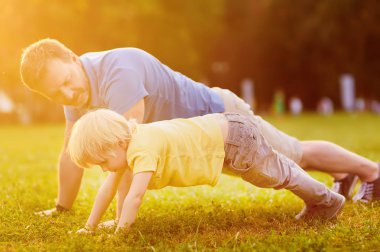 Küçük bir çocuk ve babası tahta egzersiz güneşli yaz Park yapmak. Açık spor aktiviteleri çocuklarla aile için.