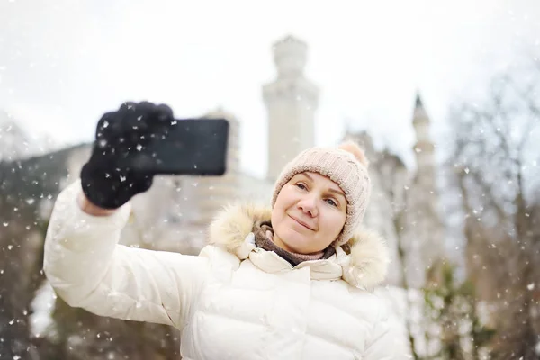 成熟した女性は 有名なロイヤル城ノイシュヴァンシュタイン城の背景に自己肖像画 Selfie を作るします 田舎で幸せな冬の週末 山での休暇 アルプス ババリア ドイツ ドイツ — ストック写真