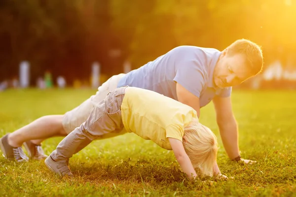 少年と彼の父親は 日当たりの良い夏の公園で板の運動を行います 子供と家族のためのアウトドア スポーツ活動 — ストック写真