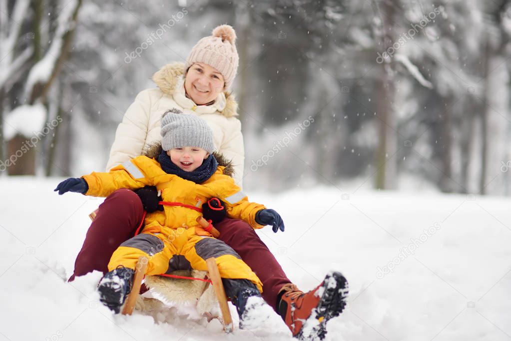 Little boy and mother/grandmother/nanny sliding in the Park during a snowfall. Outdoor winter activities for family with kids.