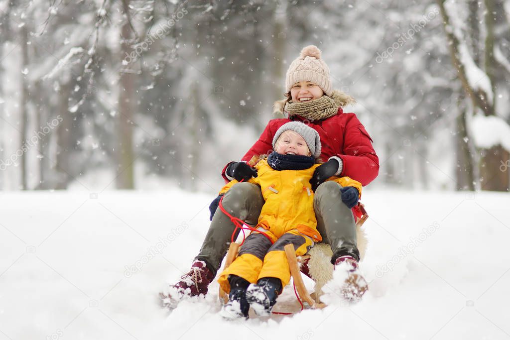 Little boy and mother sliding in the snow. Family winter activities outdoors.