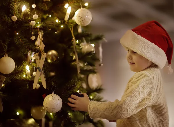 小男孩戴着圣诞老人的帽子准备庆祝圣诞节 逗人喜爱的孩子装饰圣诞树与紫色玻璃玩具 — 图库照片
