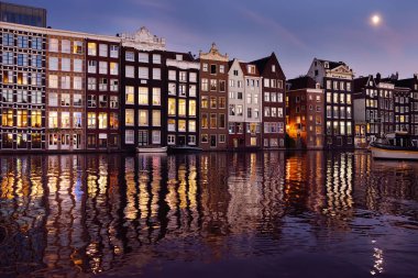 Ünlü dans Amsterdam'da Damrak kanalının gece ve Amstel Nehri'ne su onların yansıması evler