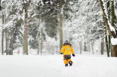 Sarı kış giysileri sevimli küçük çocuk bir kar yağışı sırasında geldi. Açık havada kış aktiviteleri çocuklar için.