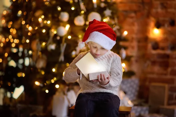 穿圣诞老人帽子的可爱小男孩打开圣诞礼物 圣诞前夜快乐孩子的肖像 舒适的客厅与装饰的冷杉树 — 图库照片