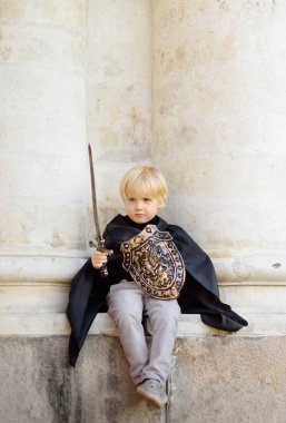 Portrait of a cute little boy dressed as a medieval knight with a sword and a shield. Medieval festival or costume party for kids clipart