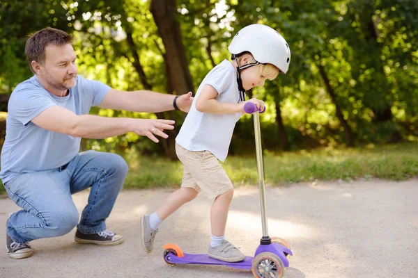 中年父亲向幼儿儿子展示如何在夏季公园骑摩托车 积极的家庭休闲 戴头盔的孩子安全 休闲与孩子的概念 — 图库照片