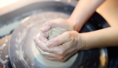 Eller kil nesneye verirseniz kadının yakın çekim fotoğraf. Bir kavanoz ya da vazo Beyaz kil seramik kurs oluşturma. Onun çalışmaları sırasında heykeltıraş. Bükülmüş potter's tekerlek.