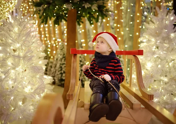 Little boy having fun and making photo on christmas installation with lights on background. Family Christmas shopping. Traditional Xmas decoration.