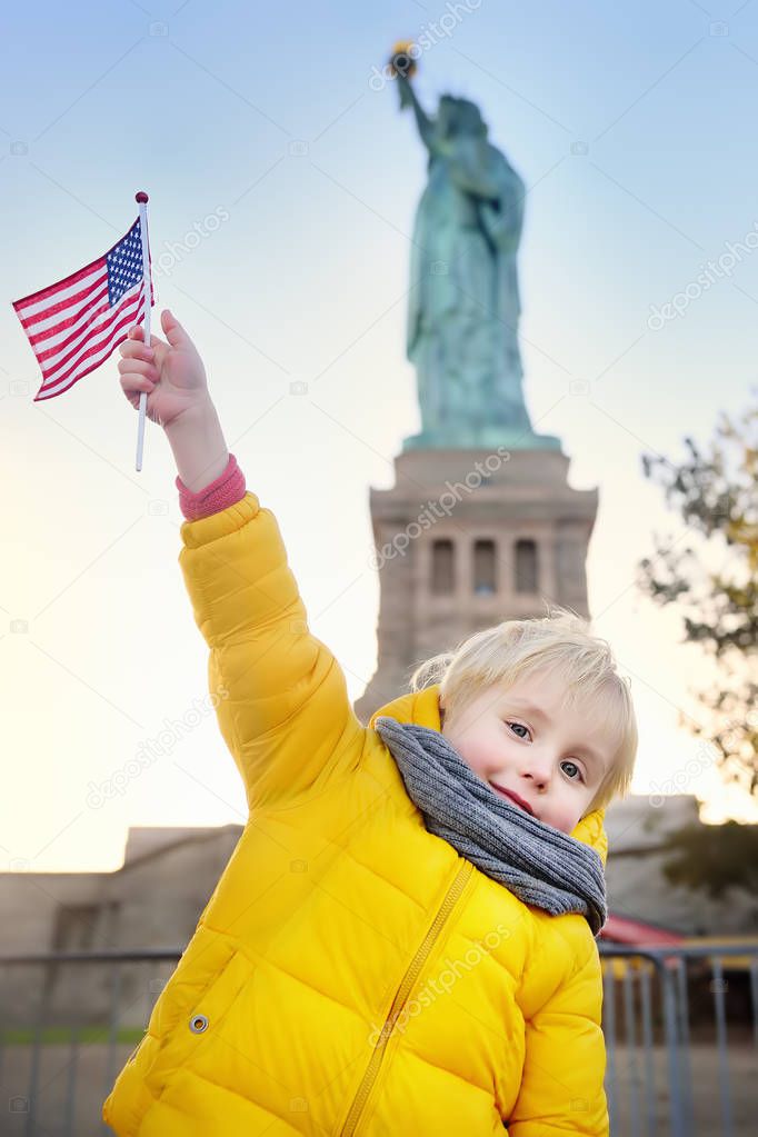 Little boy with American flag on the background of the statue of liberty in the same pose. Travel with kids.