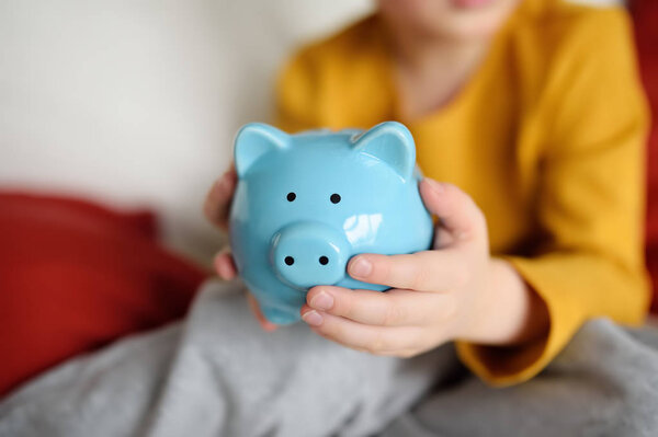 Little boy shaking a piggy moneybox and dreams of what he can buy. Education of children in financial literacy. Money saving concept.