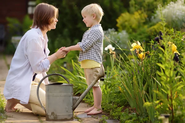 美しい若い女性と彼女のかわいい息子の夏の晴れた日に庭で植物に水をまきます 小さな子供や家族と園芸活動 — ストック写真