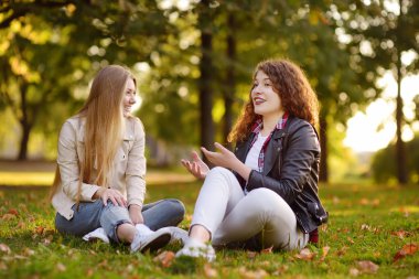 Güneşli Park yerde otururken konuşurken iki güzel genç kadın. Kız arkadaşım. İletişim ve dedikodu.