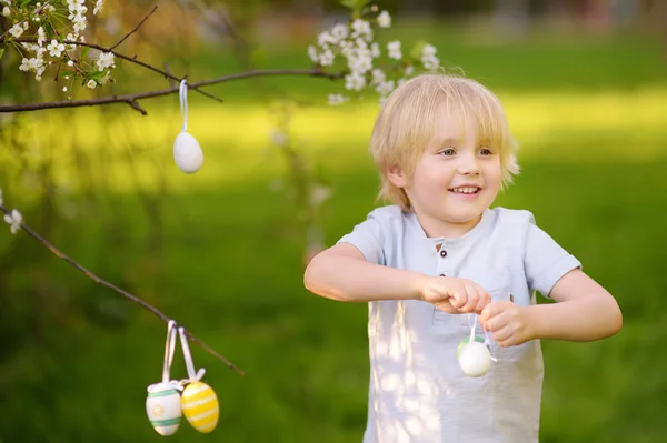 Söt liten pojke jagar påskägg på gren av blommande träd. — Stockfoto