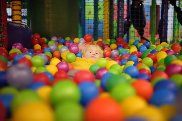 Szczęśliwy chłopiec zabawy w piłkę pit z kolorowych kulek. Dziecko gry na kryty plac zabaw dla dzieci. — Zdjęcie stockowe