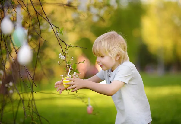 Milý chlapeček loví pro velikonoční vajíčko na větvi Kvetoucí strom. — Stock fotografie