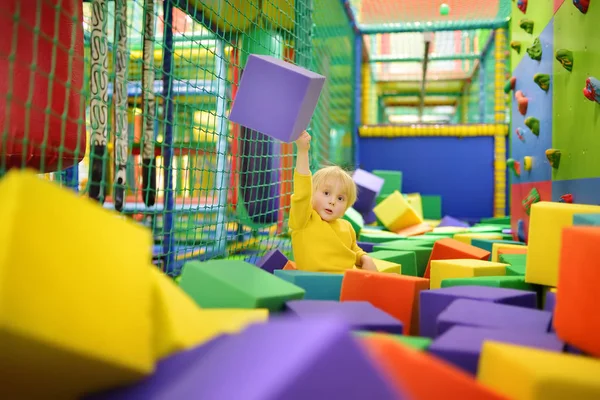 Ładny mały chłopiec bawi się miękkie kostki w suchym basenie w centrum gry. Dziecko grając na kryty plac zabaw w pit gumy piankowej w skokach na trampolinie. — Zdjęcie stockowe