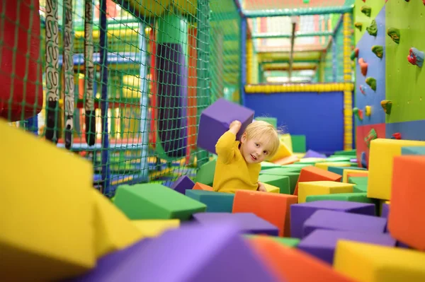 Ładny mały chłopiec bawi się miękkie kostki w suchym basenie w centrum gry. Dziecko grając na kryty plac zabaw w pit gumy piankowej w skokach na trampolinie. — Zdjęcie stockowe