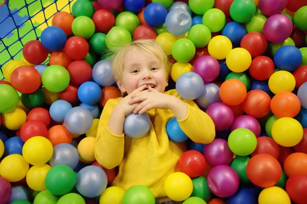 Szczęśliwy chłopiec zabawy w piłkę pit z kolorowych kulek. Dziecko gry na kryty plac zabaw dla dzieci. — Zdjęcie stockowe