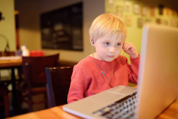 Милый мальчик смотрит мультфильм с помощью компьютера в кафе или ресторане. Детское общение через социальную сеть или мессенджер с помощью ноутбука. Дети онлайн . — стоковое фото