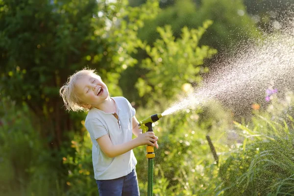 Lustiger kleiner Junge spielt mit Gartenschlauch im sonnigen Hinterhof — Stockfoto