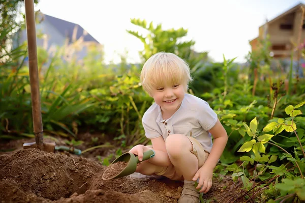 Mały chłopiec kopać łopatą w podwórku w słoneczny letni dzień. Mama małego pomocnika. — Zdjęcie stockowe