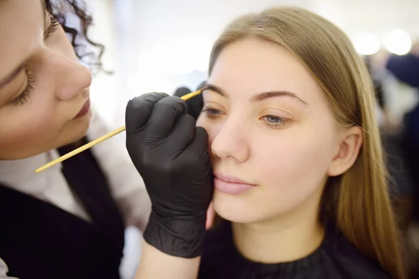 Cosmetologist pintando sobrancelhas pela escova. Mulher atraente recebendo cuidados faciais e maquiagem no salão de beleza. Sobrancelhas de arquitetura . — Fotografia de Stock