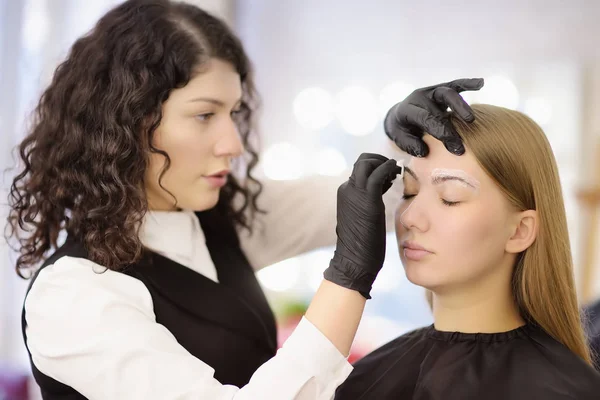 Cosmetologist que faz a composição das sobrancelhas. Mulher atraente recebendo cuidados faciais no salão de beleza. Sobrancelhas de arquitetura . — Fotografia de Stock