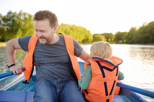 Reifer Vater und kleiner Sohn beim Bootfahren auf einem Fluss oder Teich an sonnigen Sommertagen. Qualität der gemeinsamen Familienzeit in der Natur. — Stockfoto