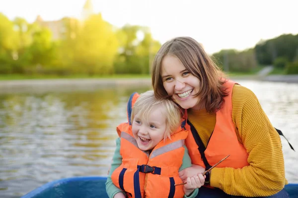 Jovem mãe e pequeno filho de barco em um rio ou lagoa no dia ensolarado de verão. Tempo de família de qualidade juntos na natureza . — Fotografia de Stock