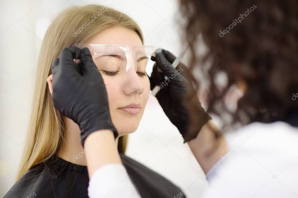 Cosmetologist making eyebrows makeup. Attractive woman getting facial care at beauty salon. Architecture eyebrows.