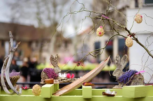 Easter decorations on the street of small town in France. Easter painted eggs hanging on a branch of tree and wooden bunny toys as decoration. — Stock Photo, Image