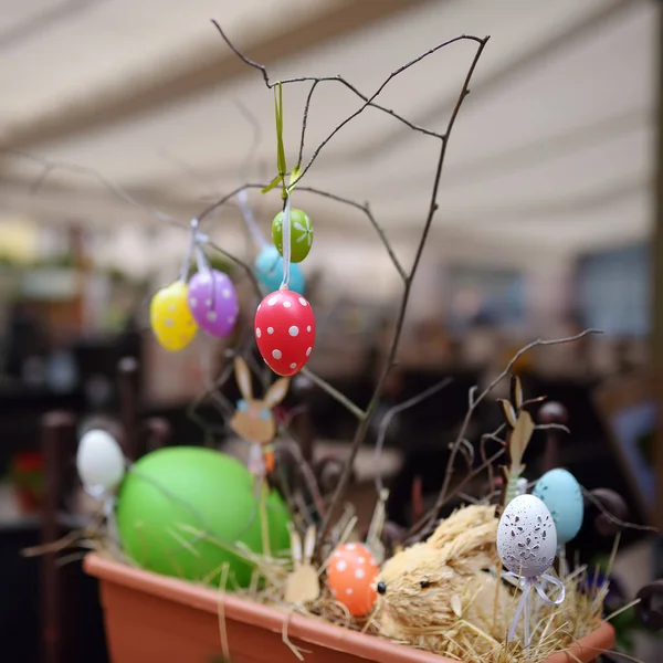 Easter decorations on the street of small town in France. Easter painted eggs hanging on a branch of tree and wooden bunny toys as decoration. — Stock Photo, Image