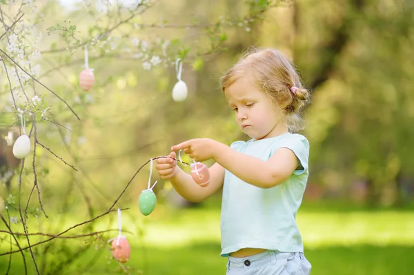 Niedliches kleines Mädchen jagt Osterei auf Ast blühenden Baum. — Stockfoto