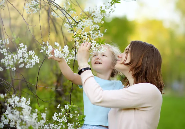 Cute Little Girl w ramionach jej pięknej matki w wiśniowym lub jabłkowym sadu podczas kwitnienia. Wielkanoc. — Zdjęcie stockowe