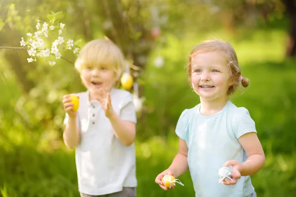 Affascinanti bambini piccoli a caccia di uova dipinte nel parco primaverile il giorno di Pasqua . — Foto Stock