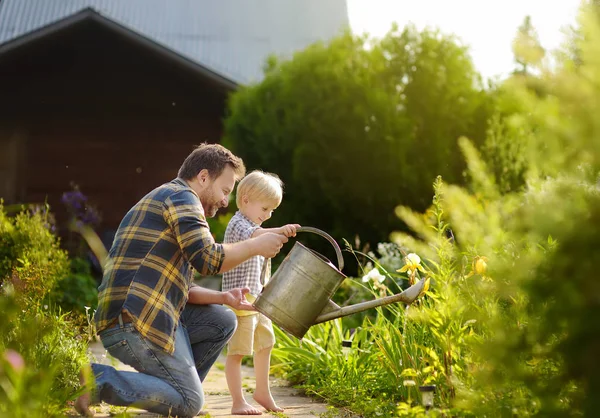 Mann mittleren Alters und sein kleiner Sohn gießen an einem sonnigen Sommertag Blumen im Garten — Stockfoto