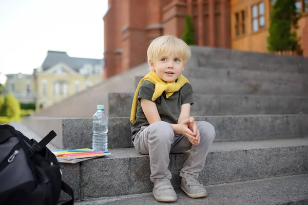 Маленький студент сидит на лестнице рядом со школьным зданием. Возвращение в школу . — стоковое фото