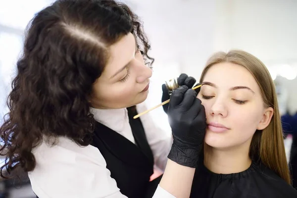 Cosmetologist pintando sobrancelhas pela escova. Mulher atraente recebendo cuidados faciais e maquiagem no salão de beleza. Sobrancelhas de arquitetura . — Fotografia de Stock