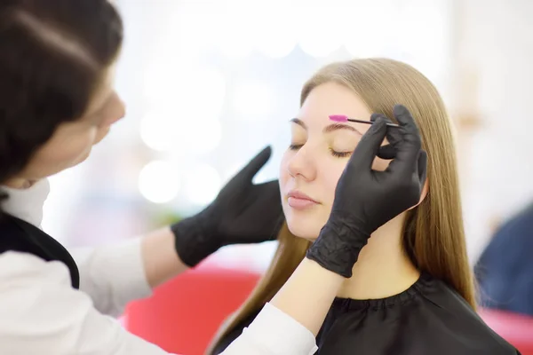 Esteticista penteia sobrancelhas usando escova especial no rosto jovem modelo bonito. Cuidados faciais e maquiagem — Fotografia de Stock