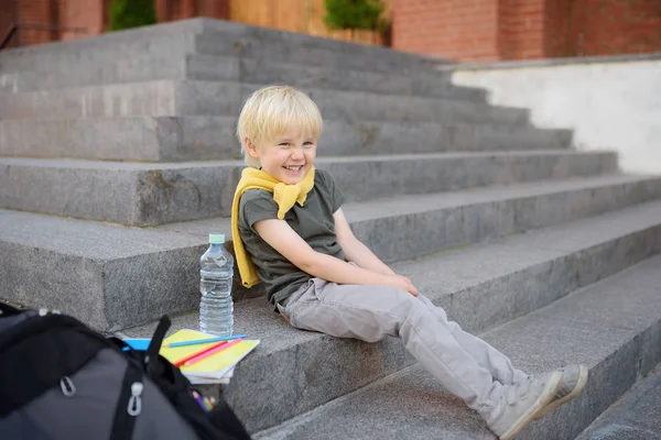Malý student sedí na schodech u školní budovy. Zpět do školy. — Stock fotografie