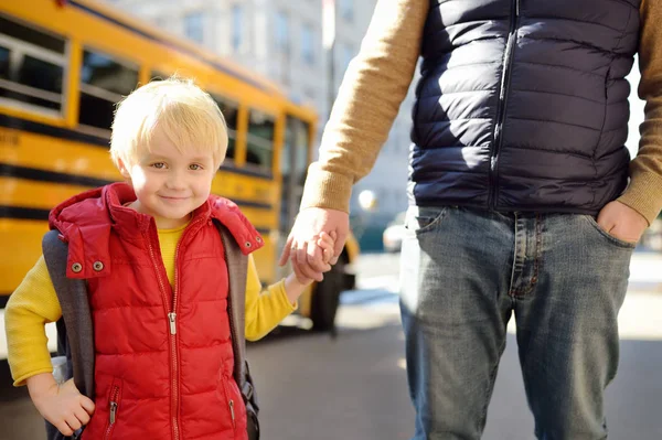 Elementary student hold hands his father near yellow school bus on background. — Stock Photo, Image