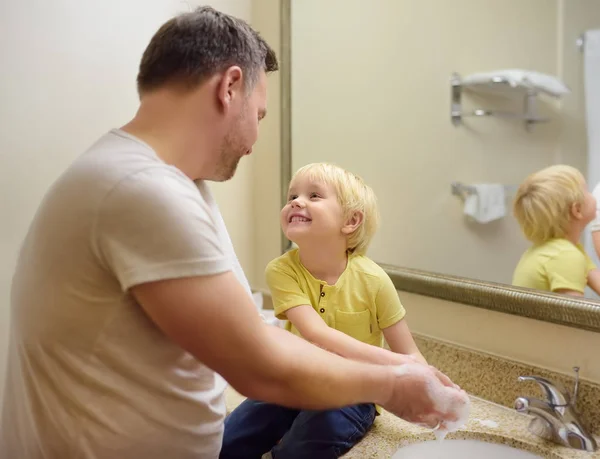 Der kleine Junge und sein Vater waschen sich im Badezimmer gemeinsam die Hände mit Seife. Hygiene für kleines Kind. — Stockfoto