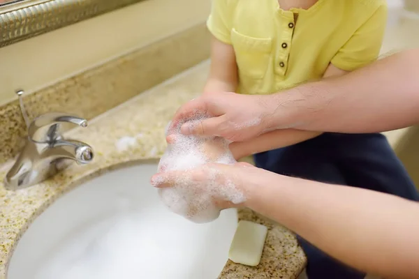 Der kleine Junge und sein Vater waschen sich im Badezimmer gemeinsam die Hände mit Seife. Hygiene für kleines Kind. — Stockfoto