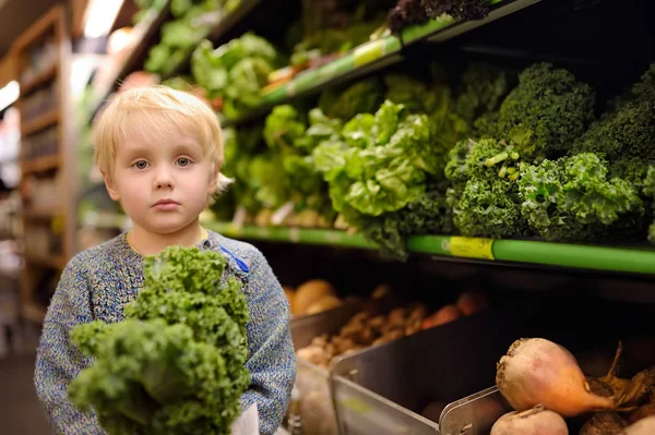 Söt småbarns pojke i en mataffär eller en stormarknad välja färsk ekologisk grönkål sallad. — Stockfoto