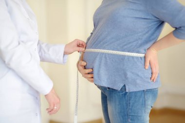 Jinekolog doktor hamile bir kadının santimetre lik bandı ile ölçer. Sağlık sigortası çocuk doğurma. Gebelik için aile doktoru. Doğum izni.