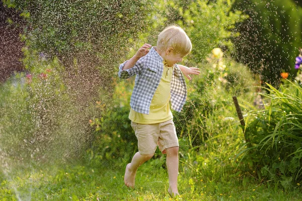 Chico divertido jugando con aspersor de jardín en el patio trasero soleado —  Fotos de Stock
